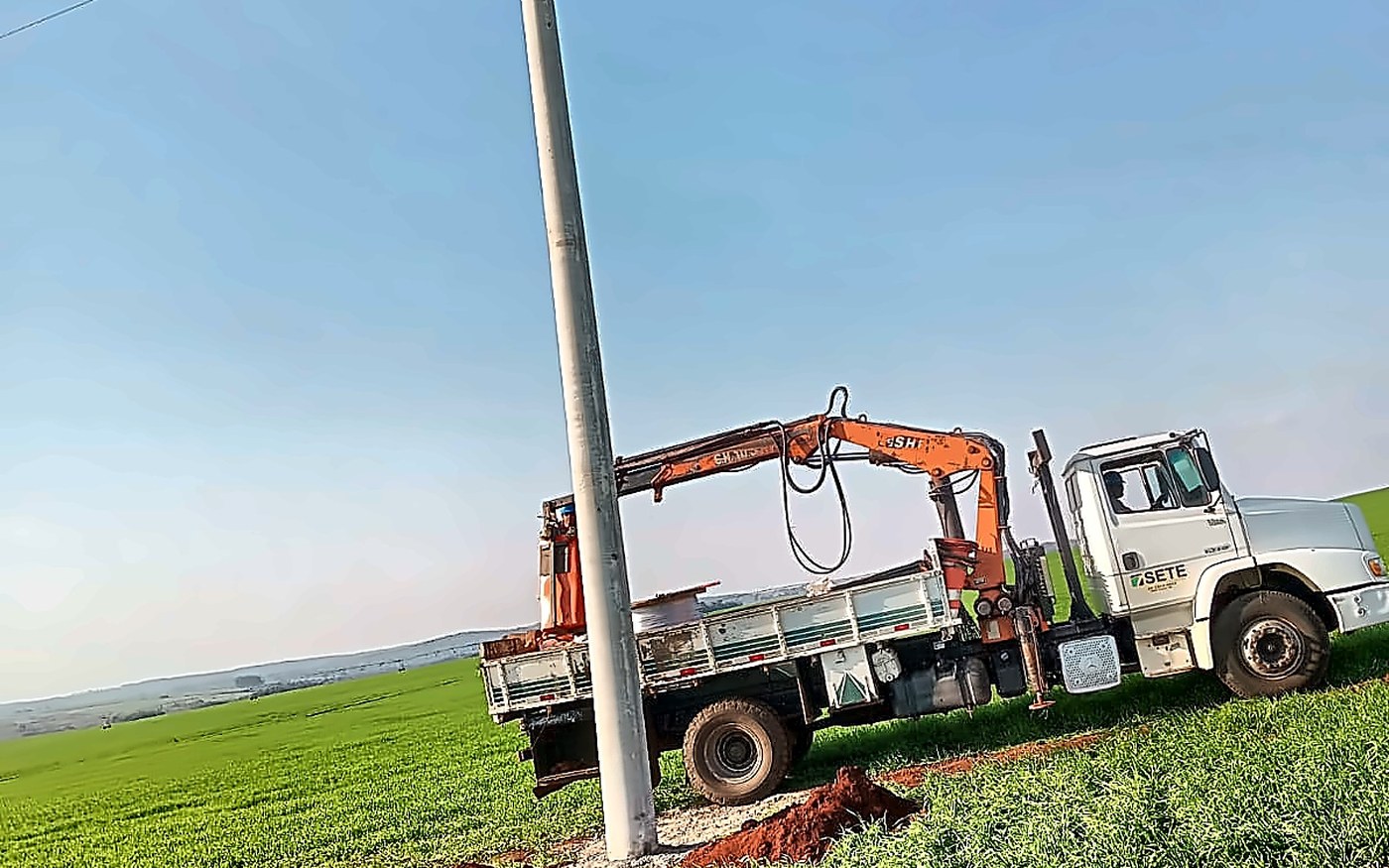 Caminhão munck da Sete Engenharia e novo poste de média tensão em propriedade rural — deslocamento de rede para a Cambaí Sementes